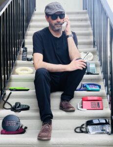 The artist N.Sputnik sits on a stairway with phones on each step, holding a cordless phone.